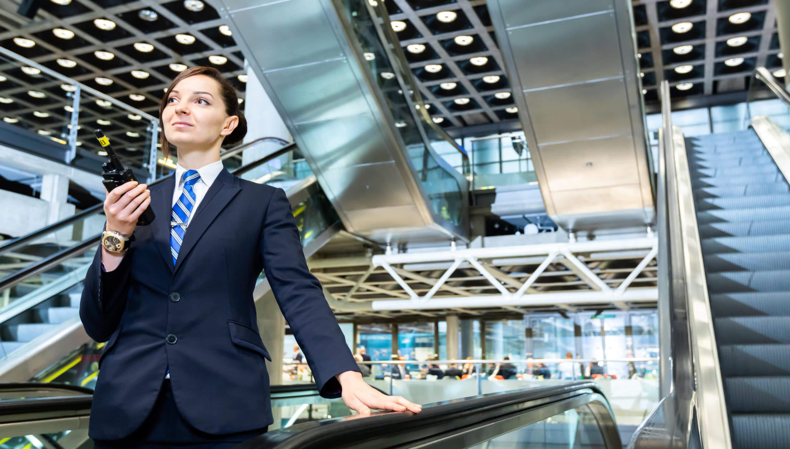 Female security officer using a radio in front of escalators