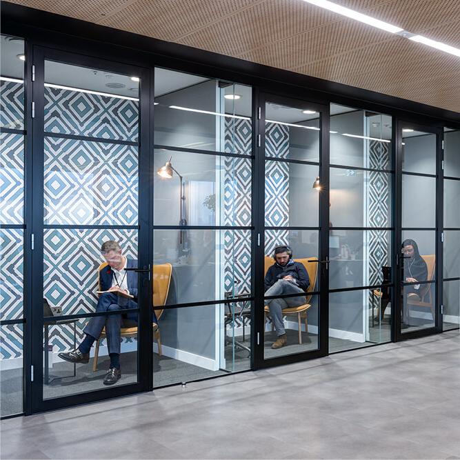 Three individual soundproofed rooms in an office for taking calls, each with a professional person inside sitting on orange chairs